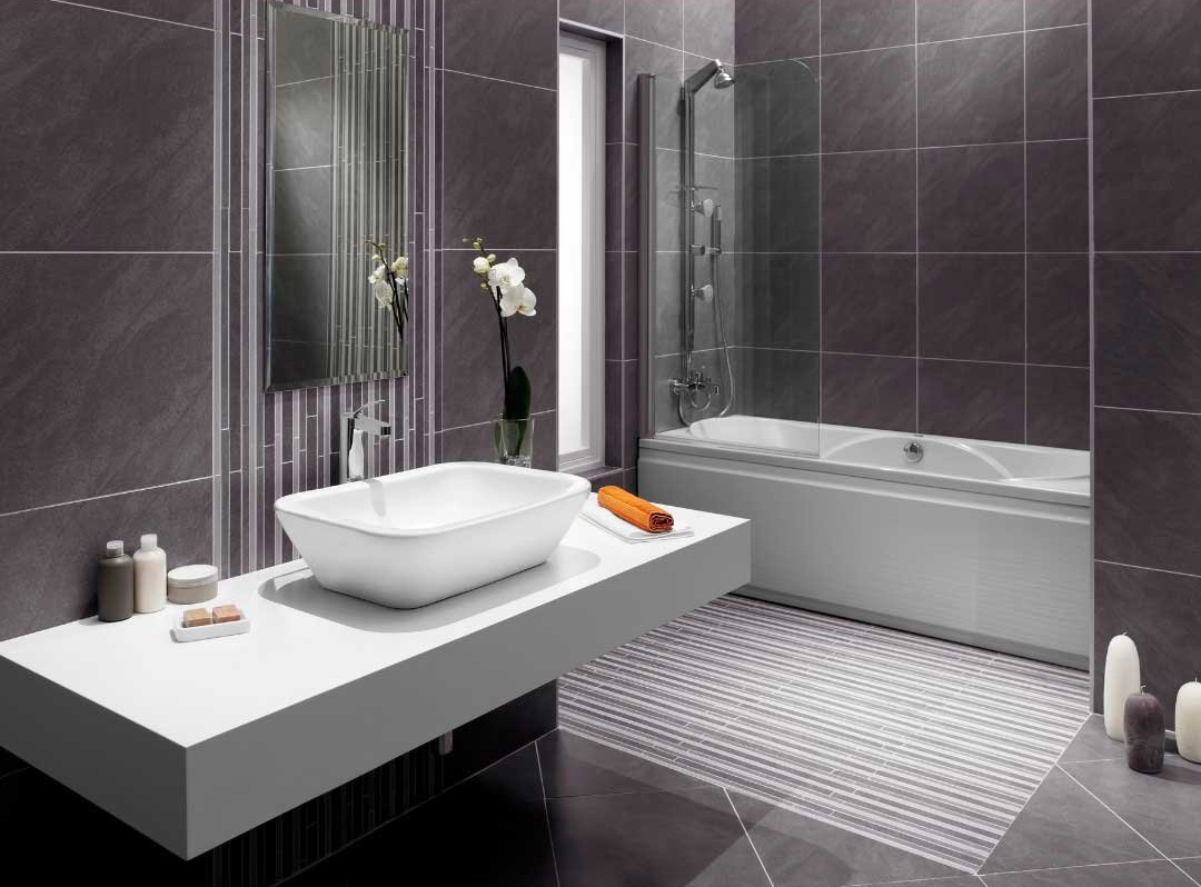 A luxurious bathroom remodeling featuring a modern design with dark gray floor-to-ceiling tiles. The space includes a sleek floating white vanity with a vessel sink, complemented by a stylish rectangular mirror and decorative elements like an orchid plant. The bathtub has a glass shower screen and is positioned against the same elegant dark gray tiles. The room is well-lit, highlighting the clean lines and sophisticated aesthetic of the remodeling. This bathroom showcases expert craftsmanship and contemporary design in remodeling.